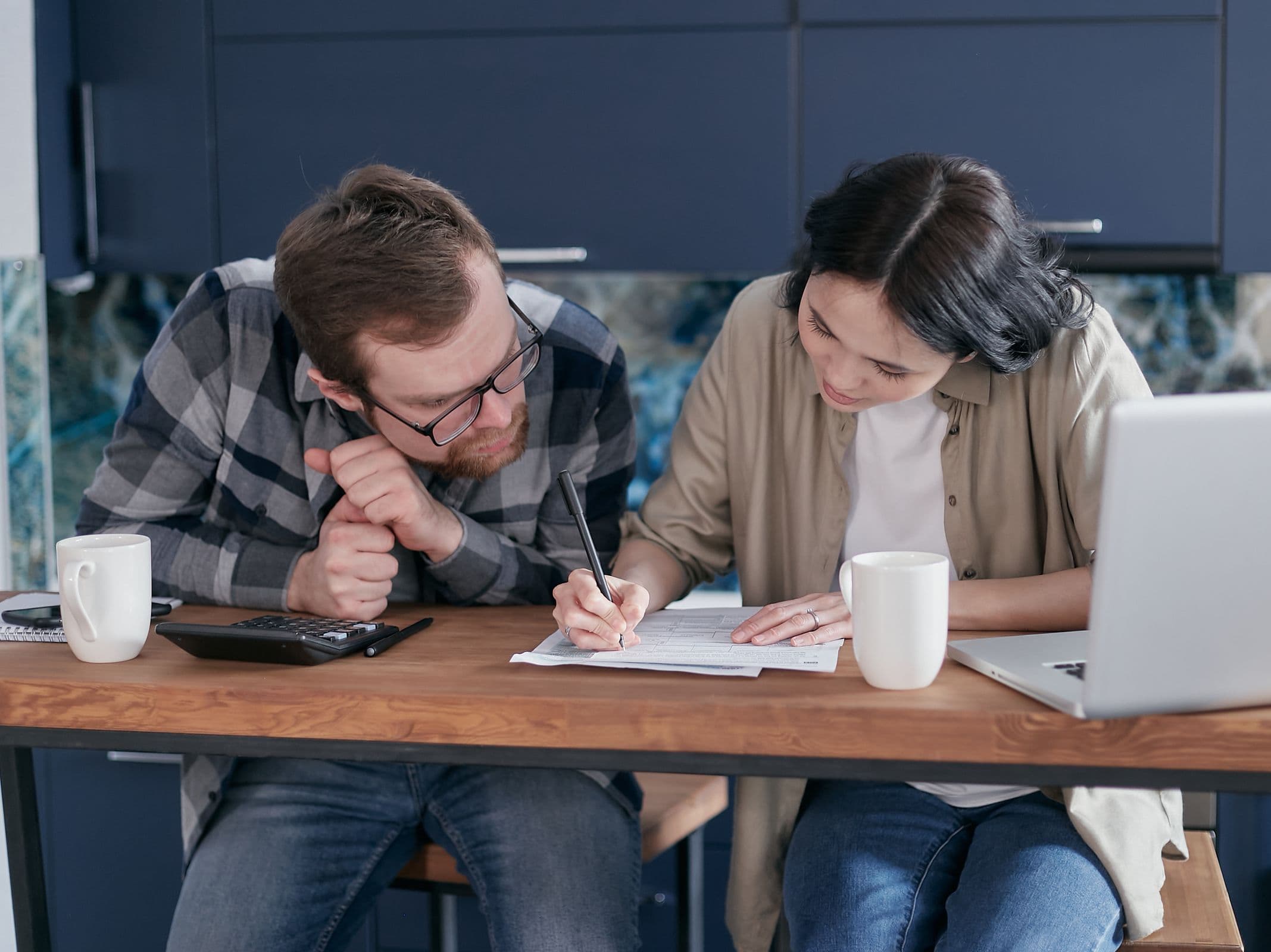 A couple reviewing financial documents together at a kitchen table with a laptop and calculator