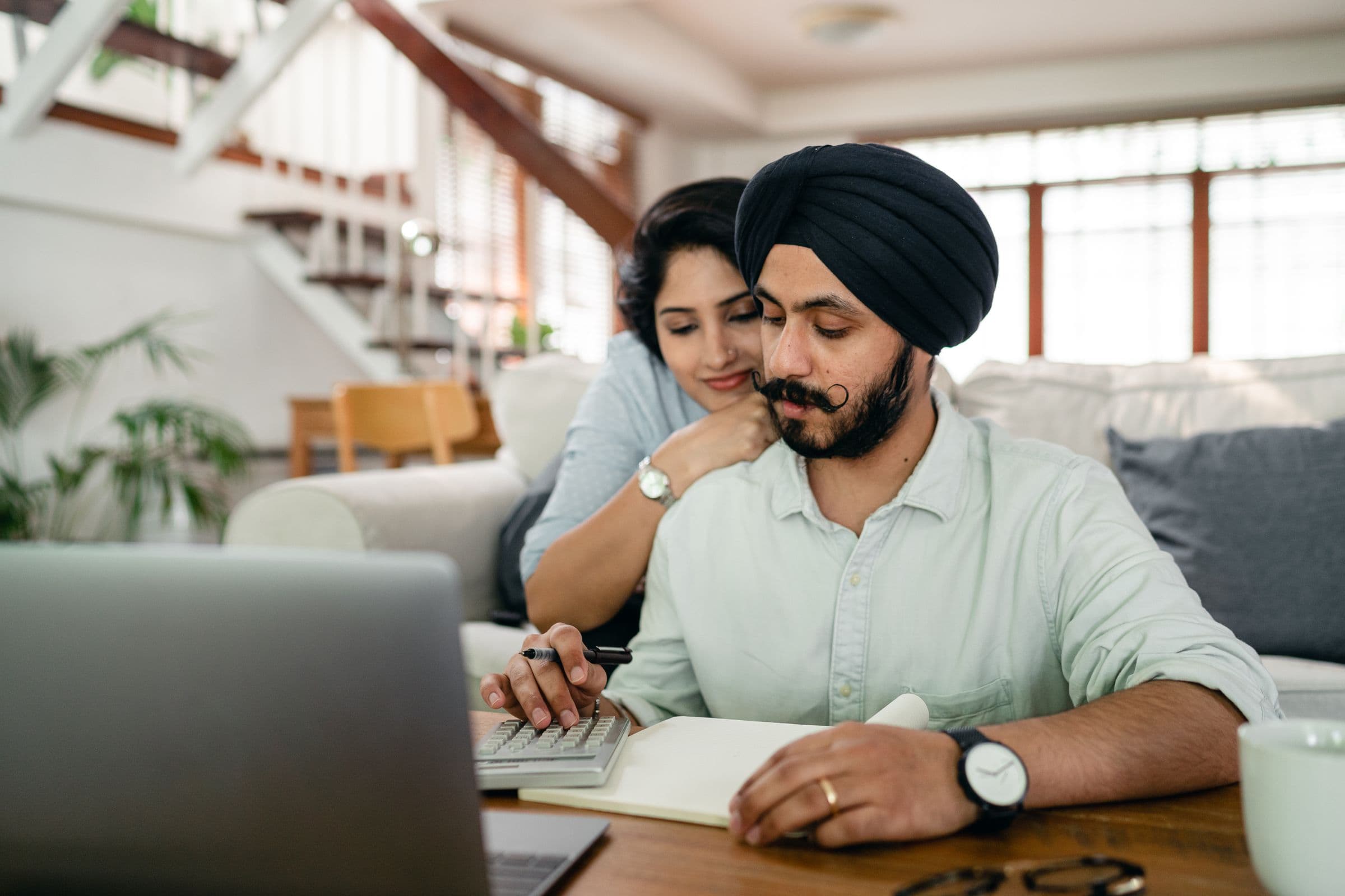 A couple smiling while using a calculator to review their savings at home
